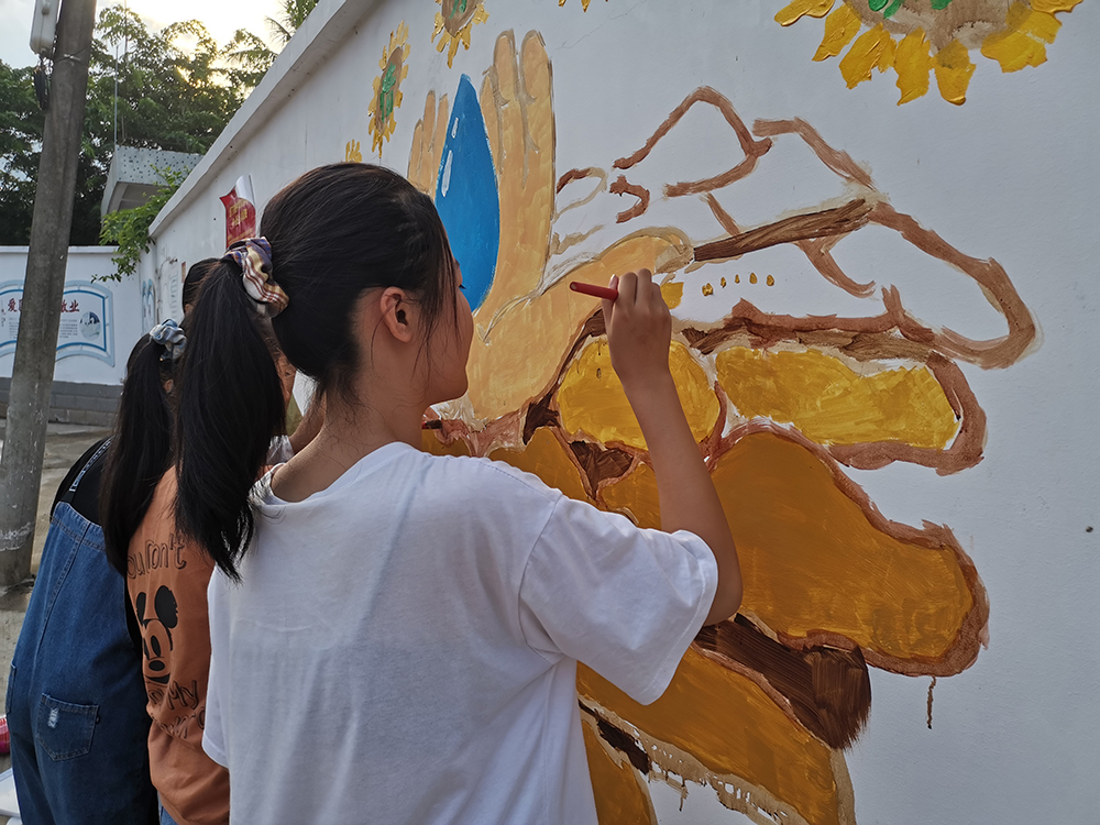 龙湖镇居丁初级中学的学生正用手中的画笔绘制环保墙绘作品.